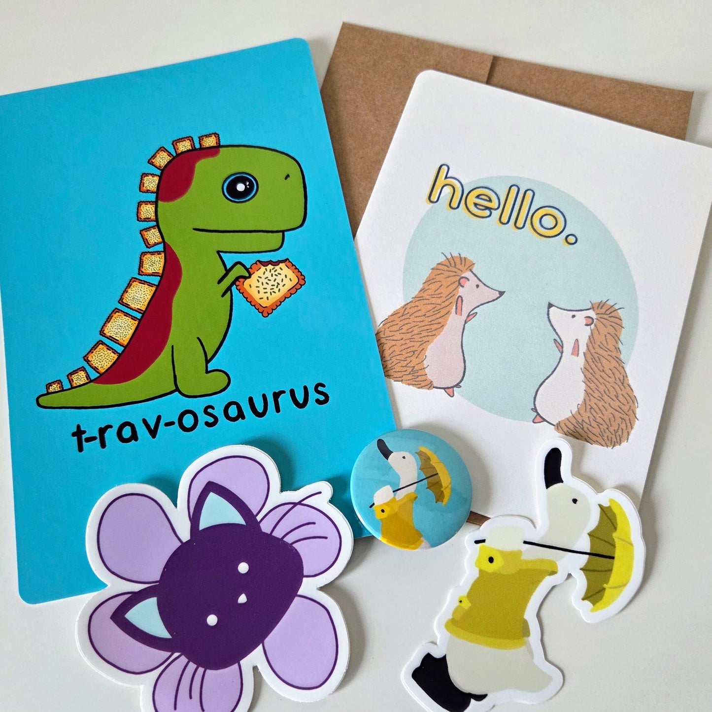 Collection of colorful stickers featuring a dinosaur, hedgehogs, flowers, a cat, and a duck with an umbrella on a white background.